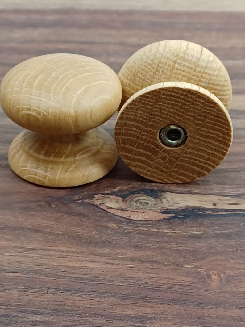 May include: Three wooden knobs with a natural finish. The knobs have a round shape with a raised center and a threaded hole in the back.