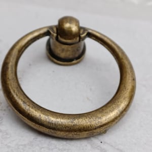 May include: A brass ring pull cabinet handle with a round knob. The handle has a smooth, slightly textured finish.