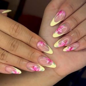 May include: Almond-shaped nails with a yellow base and clear tips. Each nail features a pink floral design with green accents. The nails are long and well-manicured, showcasing a delicate and artistic nail art style.