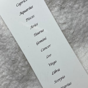 May include: A white card with the twelve zodiac signs listed in order: Capricorn, Aquarius, Pisces, Aries, Taurus, Gemini, Cancer, Leo, Virgo, Libra, Scorpio, Sagittarius.