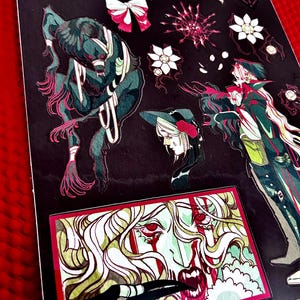 May include: A sheet of stickers featuring various gothic-themed illustrations. The designs include a monster, a woman with long hair, and floral accents, all in a dark color palette with red and pink highlights. The stickers are on a black background.