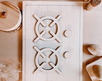 May include: A wooden toy stovetop with two burner elements. The stovetop is made of light wood and has a simple design. The burners are round and have a cross-shaped design in the center.