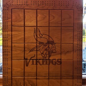 May include: Wooden cribbage board with the text "RICE" and "Minnesota Vikings" engraved at the top. The board features a grid pattern and a Viking logo in the center. The board is made of wood and has a natural finish.