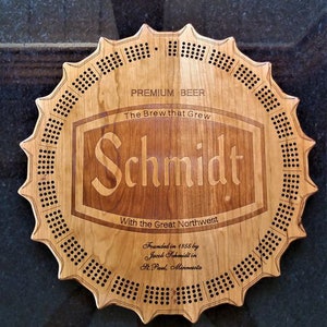 May include: A wooden cribbage board shaped like a beer bottle cap with the Schmidt Brewery logo and text: "Premium Beer, The Brew that Grew, With the Great Northwest, Founded in 1855 by Jacob Schmidt in St. Paul, Minnesota".