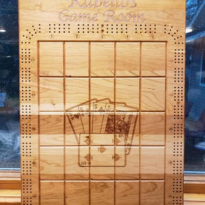 May include: A wooden game board with a grid pattern and the text "Rabello's Game Room" engraved on the top. The board has a design of playing cards in the center.