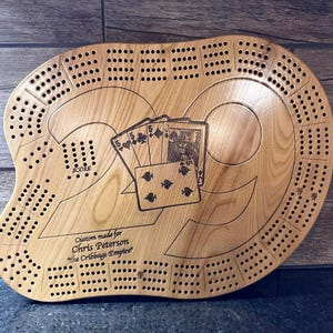 May include: Wooden cribbage board with a unique design. The board features a carved number 29, playing cards, and numerous holes for pegs. Text on the board reads "Custom made for Chris Peterson 'The Cribbage Empire'".