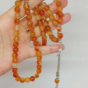 May include: A string of orange carnelian prayer beads with silver accents. The beads are round and have a smooth, polished finish. The string is approximately 33 inches long.