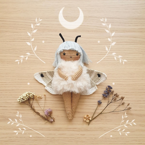 Puede incluir: Una muñeca de crochet con un diseño de mariposa blanco y azul claro. La muñeca tiene una falda de piel blanca y lleva una diadema blanca. La muñeca está sentada sobre una superficie de madera.