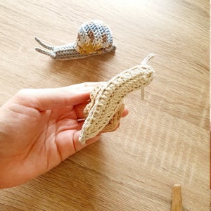 May include: Two crocheted snails, one beige and one with a blue, brown, and yellow shell.