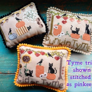 May include: Three small, square, cream-colored pillows with black and orange embroidery. The pillows are decorated with a black cat, pumpkins, and the words "Cider Tyme", "Pumpkin Tyme", and "Punkin Tyme".