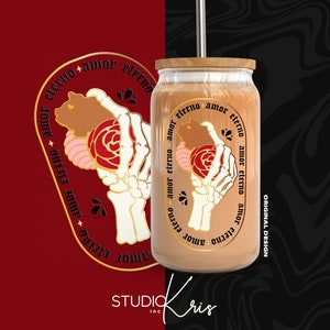 May include: A gold and black tumbler with a skeletal hand holding a rose and a bear. The tumbler has the text "amor eterno" repeated around the design. The tumbler is on a black and white background.
