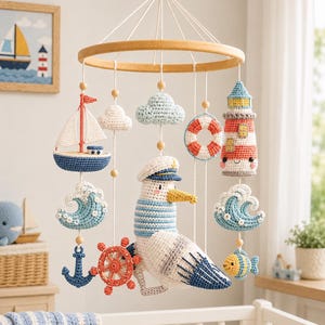 May include: A nautical-themed mobile featuring crocheted figures suspended from a wooden ring. The elements include a sailboat, a lighthouse, a seagull wearing a captain's hat, a lifebuoy, a ship's wheel, an anchor, clouds, waves, and a small fish.