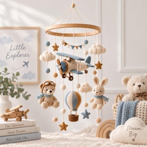 Puede incluir: Un móvil de ganchillo para bebé con un marco de madera circular del que cuelgan un avión beige y azul, un oso de peluche con gafas, un globo aerostático, un conejo con bufanda azul, nubes, estrellas y pequeñas esferas en azul y beige.