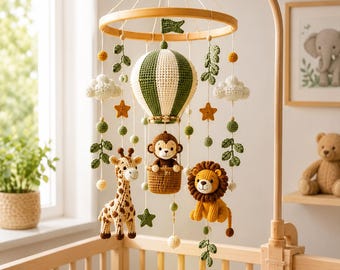 May include: A nursery mobile featuring a crocheted hot air balloon in green and white, a monkey in a basket, a giraffe, and a lion. The mobile includes crocheted clouds, stars, and leaf vines suspended from a circular wooden frame on a stand.