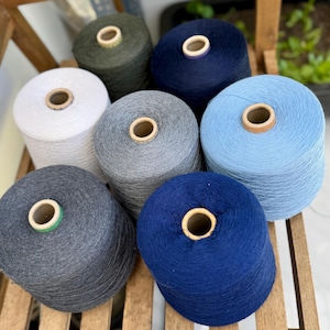 Peut inclure: Sept bobines de fil cylindriques disposées en groupe. Les couleurs incluent le vert olive, le bleu marine foncé, le blanc, le gris clair, le bleu clair, le gris anthracite et le bleu roi. Chaque bobine possède un noyau central en carton.