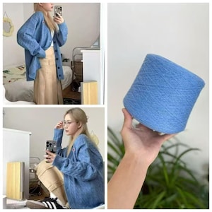 May include: A light blue cable knit cardigan with a button-down front and a matching cone of light blue yarn. The cardigan features long sleeves, a V-neckline, and a small rectangular patch on the chest. The yarn is wound into a dense cylinder.