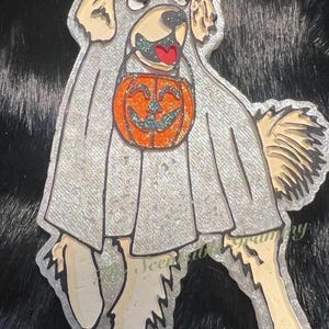 May include: A glittery dog-shaped Halloween decoration. The dog is dressed as a ghost, with a pumpkin on its chest. The dog is light brown and beige, with a red tongue. The ghost costume is silver.