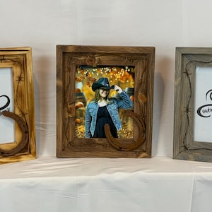 May include: Three wooden picture frames with a rustic cowboy theme. Each frame has a horseshoe accent and barbed wire detailing. The frames are in shades of brown and gray, with the center frame holding a photo of a person.