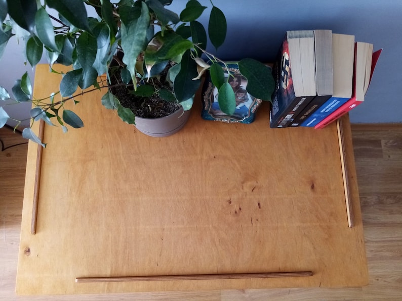 May include: A rectangular light brown wooden tray with a smooth surface and thin raised wooden edges on three sides. The tray is positioned horizontally, featuring a natural wood grain pattern and a simple, functional design for holding various items.