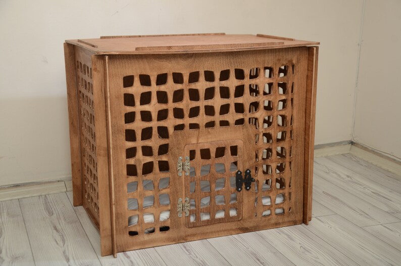 K&ouml;nnte beinhalten: Eine rechteckige Haustierbox aus Holz mit mittelbraunem Finish und einem gitterartigen Ausschnittmuster an allen Seiten. Die Vorderseite verf&uuml;gt &uuml;ber eine Fl&uuml;gelt&uuml;r mit silberfarbenen Metallscharnieren und einem schwarzen Riegel.