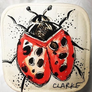 May include: A white fabric hot pad featuring a black and red ladybug illustration. The ladybug has black spots and the artist's signature "CLARKE" is in the bottom right corner.