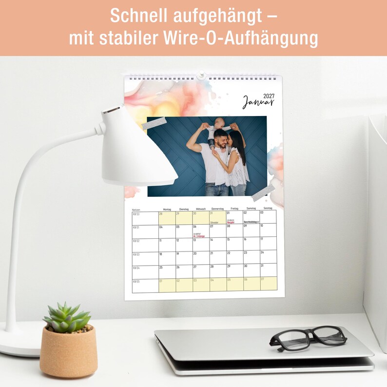 May include: A 2027 wall calendar featuring a photograph of a family with a child on shoulders, watercolor accents, and a grid for January. The text reads "Schnell aufgeh&auml;ngt &ndash; mit stabiler Wire-O-Aufh&auml;ngung" and "2027 Januar" at the top of the page.