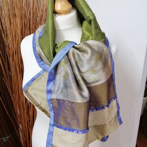 May include: A green, blue and beige silk scarf with a patchwork design. The scarf is tied around a mannequin's neck.