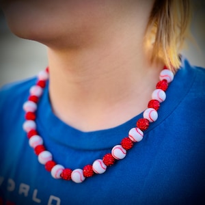 May include: A white and red baseball-themed necklace with white beads and red glitter accents.