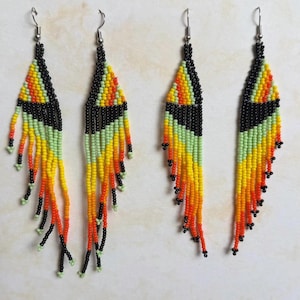 May include: Handmade beaded earrings with a geometric design. The earrings feature a black top section, transitioning to yellow, orange, and green fringe. The fringe is accented with black beads. The earrings are labeled with the numbers 18 and 19.