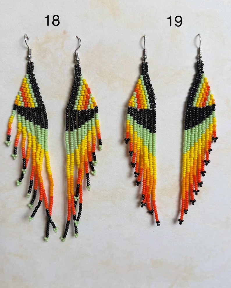 May include: Handmade beaded earrings with a geometric design. The earrings feature a black top section, transitioning to yellow, orange, and green fringe. The fringe is accented with black beads. The earrings are labeled with the numbers 18 and 19.