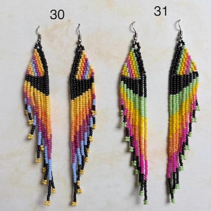 May include: Two pairs of beaded earrings. One pair features a black triangle design with orange, yellow, pink, and blue beads. The other pair has a black triangle design with yellow, green, and pink beads. Both pairs have silver hooks.