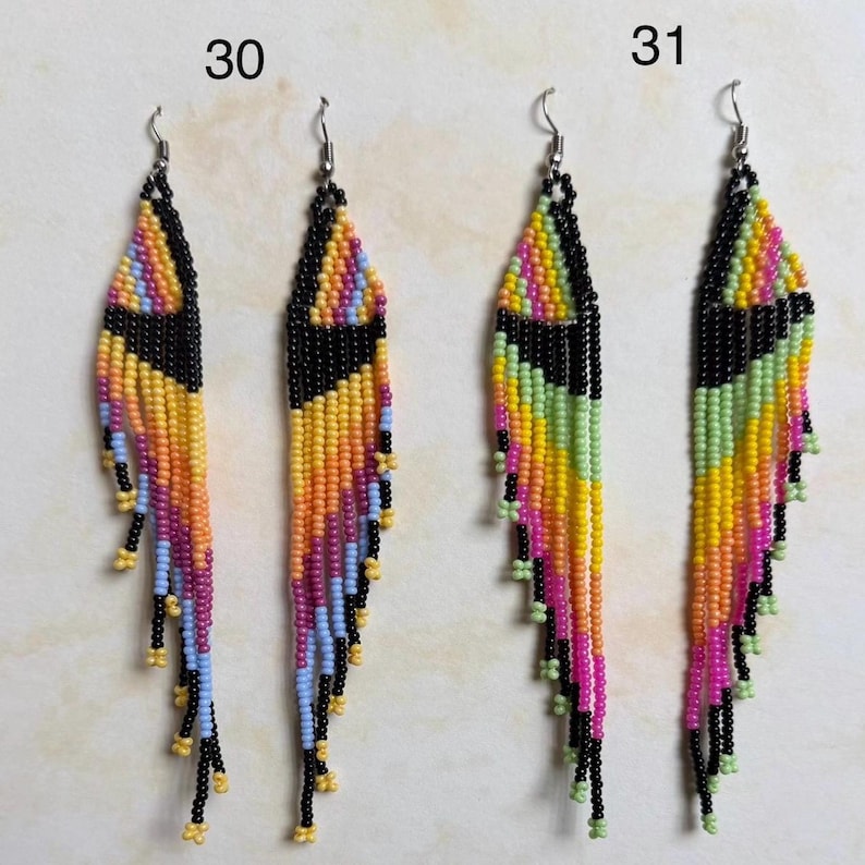 May include: Two pairs of beaded earrings. One pair features a black triangle design with orange, yellow, pink, and blue beads. The other pair has a black triangle design with yellow, green, and pink beads. Both pairs have silver hooks.