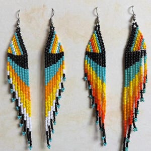 May include: Handmade beaded earrings in a feather design. The earrings feature a black top section, followed by turquoise, yellow, and orange beads. The bottom of the earrings have black and turquoise beads. The earrings are approximately 4 inches long.