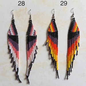 May include: Two pairs of beaded earrings. One pair features pink, white, black, and purple beads. The other pair has orange, yellow, black, and purple beads. Both pairs have silver-tone ear wires and a fringe design.