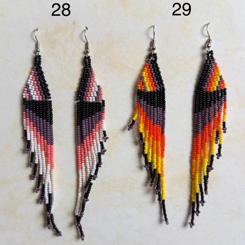 May include: Two pairs of beaded earrings. One pair features pink, white, black, and purple beads. The other pair has orange, yellow, black, and purple beads. Both pairs have silver-tone ear wires and a fringe design.