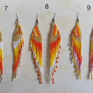 May include: Handmade beaded earrings in a feather design. The earrings feature a gold top with a gradient of colors including orange, yellow, white, and red. The earrings have a fringe of beads at the bottom.