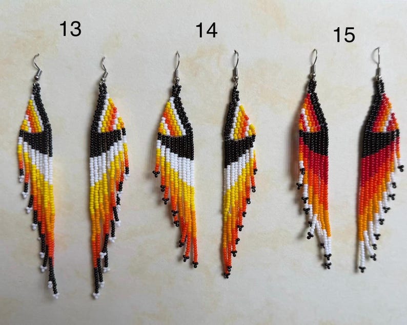 May include: A set of three pairs of beaded earrings. Each earring features a long, fringed design with a black top, and a pattern of white, yellow, orange, and red beads. The earrings are numbered 13, 14, and 15.