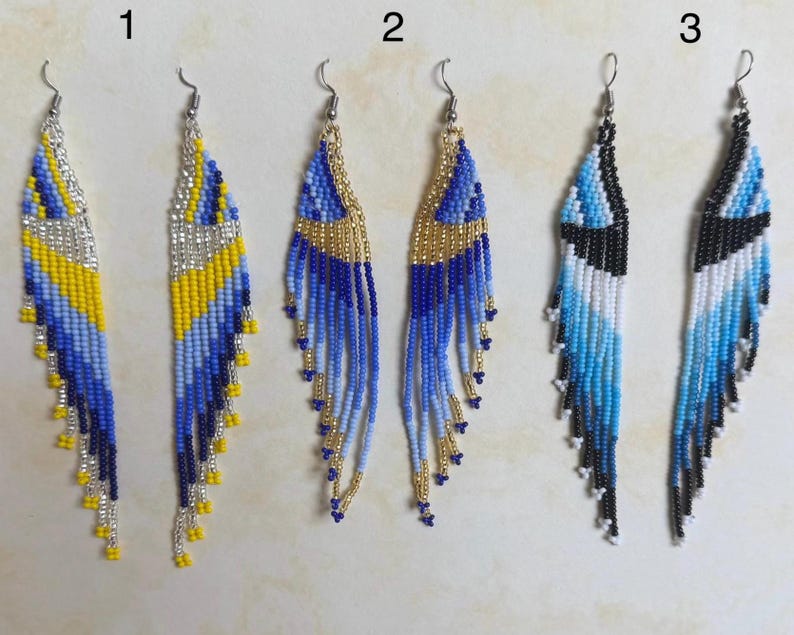 May include: Three pairs of beaded dangle earrings. The earrings feature intricate patterns in blue, yellow, silver, black, and white. Each pair has a unique design, with variations in color and bead arrangement. The earrings have silver-tone hooks.