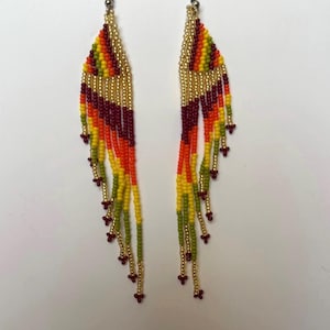 May include: A pair of beaded earrings with a colorful design. The earrings feature a gold-colored top section with a fringe of beads in shades of yellow, orange, red, and green. The earrings are approximately 4 inches long.