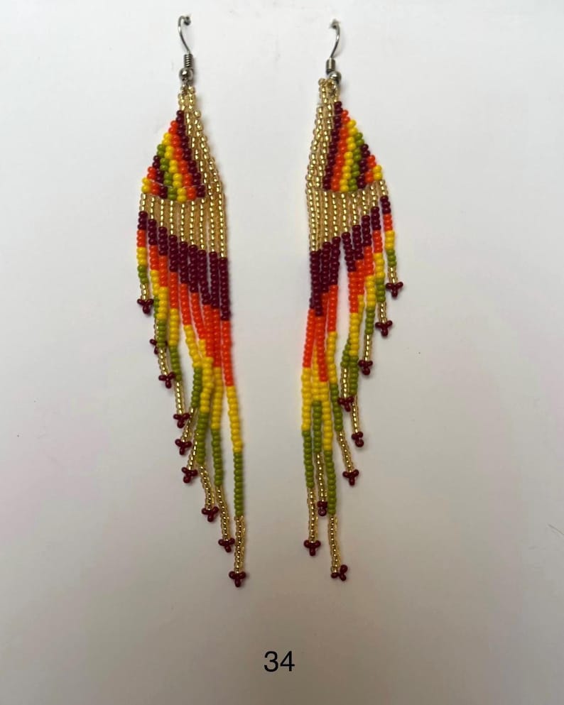 May include: A pair of beaded earrings with a colorful design. The earrings feature a gold-colored top section with a fringe of beads in shades of yellow, orange, red, and green. The earrings are approximately 4 inches long.