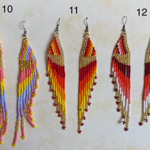 May include: Three pairs of beaded dangle earrings. The earrings feature a variety of colors, including pink, yellow, orange, red, and gold. Each earring has a gold-colored top and a fringe of beads. The earrings are designed for pierced ears.