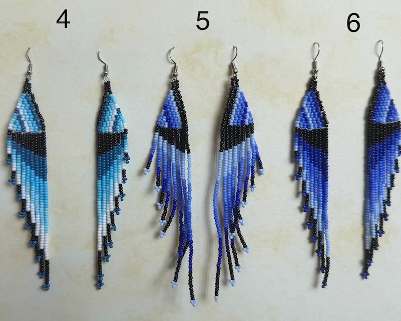 May include: A collection of six beaded earrings in shades of blue, black, and white. The earrings feature a geometric design with a fringe of beads at the bottom. Each earring has a silver-colored hook.