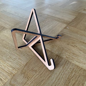 May include: A wooden laptop stand with a black trim. The stand is made of two triangles that intersect to create a stable base.