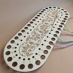 Könnte beinhalten: Ein hölzerner Fadenhalter mit 40 Löchern, die von 1 bis 40 nummeriert sind. Der Halter hat ein florales Design und wird verwendet, um mehrere Fäden für Stickerei oder andere Handarbeiten zu halten.
