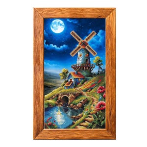 May include: A framed cross-stitch picture of a windmill on a hill under a full moon. The scene includes a small house, a bridge, and a body of water, with red flowers in the foreground. The frame is made of wood.
