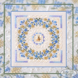 Op de afbeelding: Een witte linnen stof met een blauw en gouden geborduurd ontwerp van een bloemenkrans. De borduurwerk bevat kleine blauwe bloemen, groene bladeren en gouden accenten. De stof is omgeven door een blauwe rand.