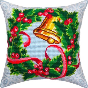 May include: A white pillow with a green holly wreath and red berries, a gold bell, and a red ribbon. The pillow is decorated with a wintery snowflake pattern.
