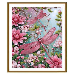 May include: A framed artwork featuring two pink dragonflies amidst pink and white flowers, green leaves, and pearl-like accents. The background is a soft blue and green with a light source. The artwork is framed in a gold-colored frame.