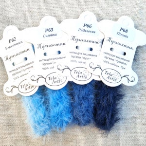 Peut inclure: Quatre bobines de fil bleu et duveteux pour la broderie. Les bobines sont étiquetées avec le texte "P62 Blakitnik", "P63 Sizoika", "P66 Rybalochka" et "P68 Pingvin". Chaque bobine est étiquetée "Puhastik" et comprend le texte "Nitka dlya vyshivaniya pir'yatih i puhnatih 100% neylon" et le logo "Tela Artis".