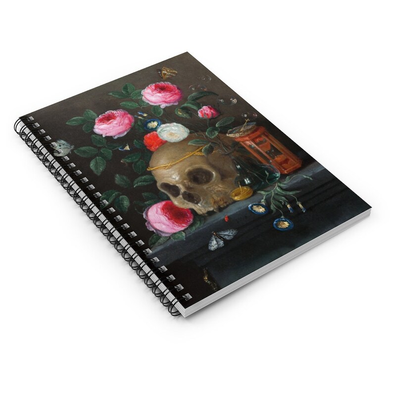 May include: Spiral-bound notebook featuring a still life painting with a skull, roses, and butterflies. The artwork has a dark background with a skull adorned with a gold chain, surrounded by pink, red, and white roses. A small hourglass and other objects are also present.